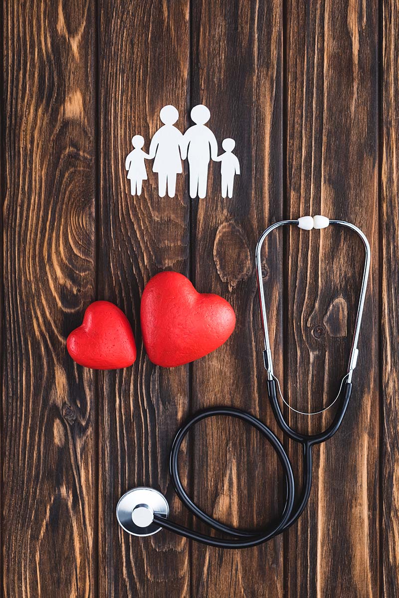 top view of white figures of family holding hands, red hearts symbols and stethoscope